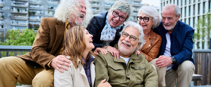 A group of elderly people sit on a bench and laugh